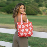 Woman with tote bag with beige and pink hibiscus print on orange red ground.