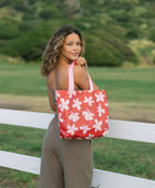 Woman with tote bag with beige and pink hibiscus print on orange red ground.