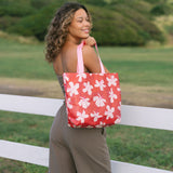 Woman with tote bag with beige and pink hibiscus print on orange red ground.