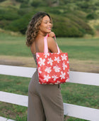 Woman with tote bag with beige and pink hibiscus print on orange red ground.