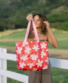 Woman with tote bag with beige and pink hibiscus print on orange red ground.