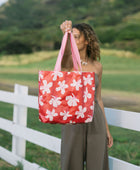 Woman with tote bag with beige and pink hibiscus print on orange red ground.