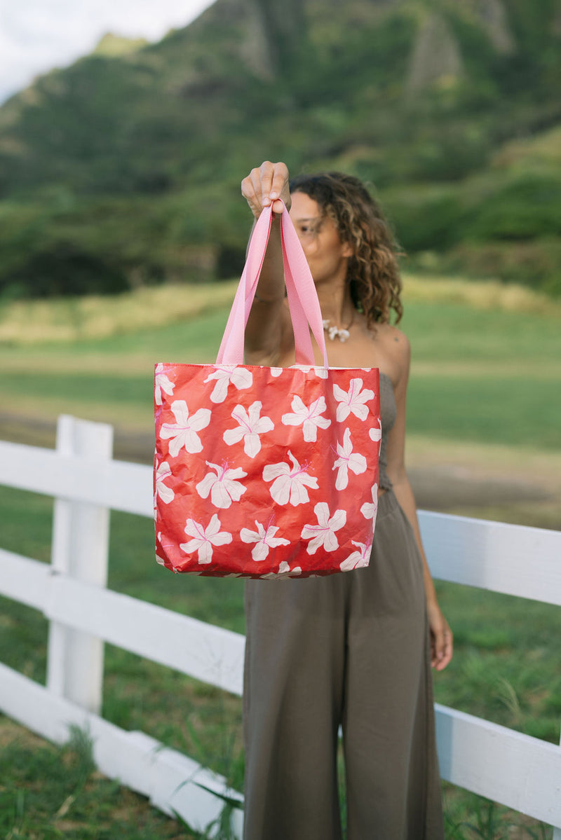 Woman with tote bag with beige and pink hibiscus print on orange red ground.