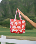 Woman with tote bag with beige and pink hibiscus print on orange red ground.