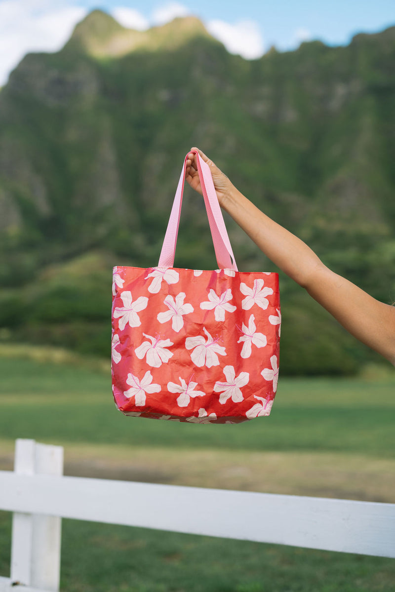 Woman with tote bag with beige and pink hibiscus print on orange red ground.