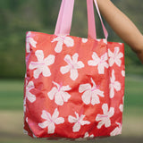 Tote bag with beige and pink hibiscus print on orange red ground.