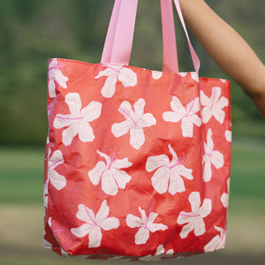 Tote bag with beige and pink hibiscus print on orange red ground.