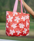 Tote bag with beige and pink hibiscus print on orange red ground.