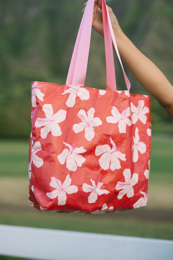 Tote bag with beige and pink hibiscus print on orange red ground.