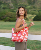 Woman with tote bag with beige and pink hibiscus print on orange red ground.