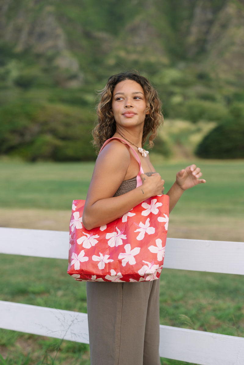 Woman with tote bag with beige and pink hibiscus print on orange red ground.