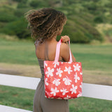 Woman with tote bag with beige and pink hibiscus print on orange red ground.