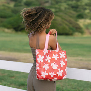 Woman with tote bag with beige and pink hibiscus print on orange red ground.
