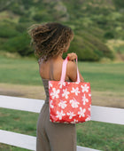 Woman with tote bag with beige and pink hibiscus print on orange red ground.