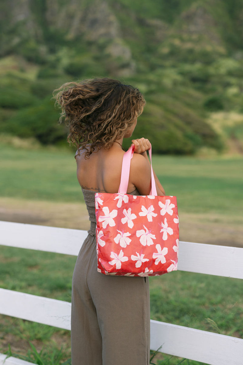 Woman with tote bag with beige and pink hibiscus print on orange red ground.