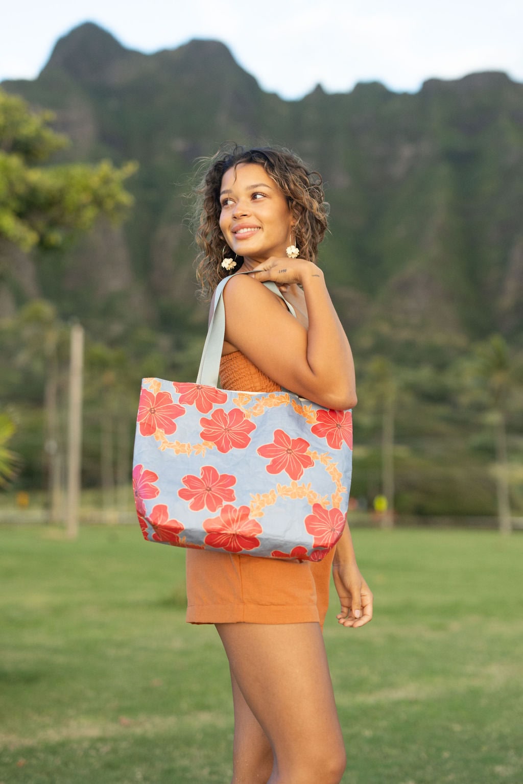 Woman with tote bag with red and orange floral print on light blue ground.
