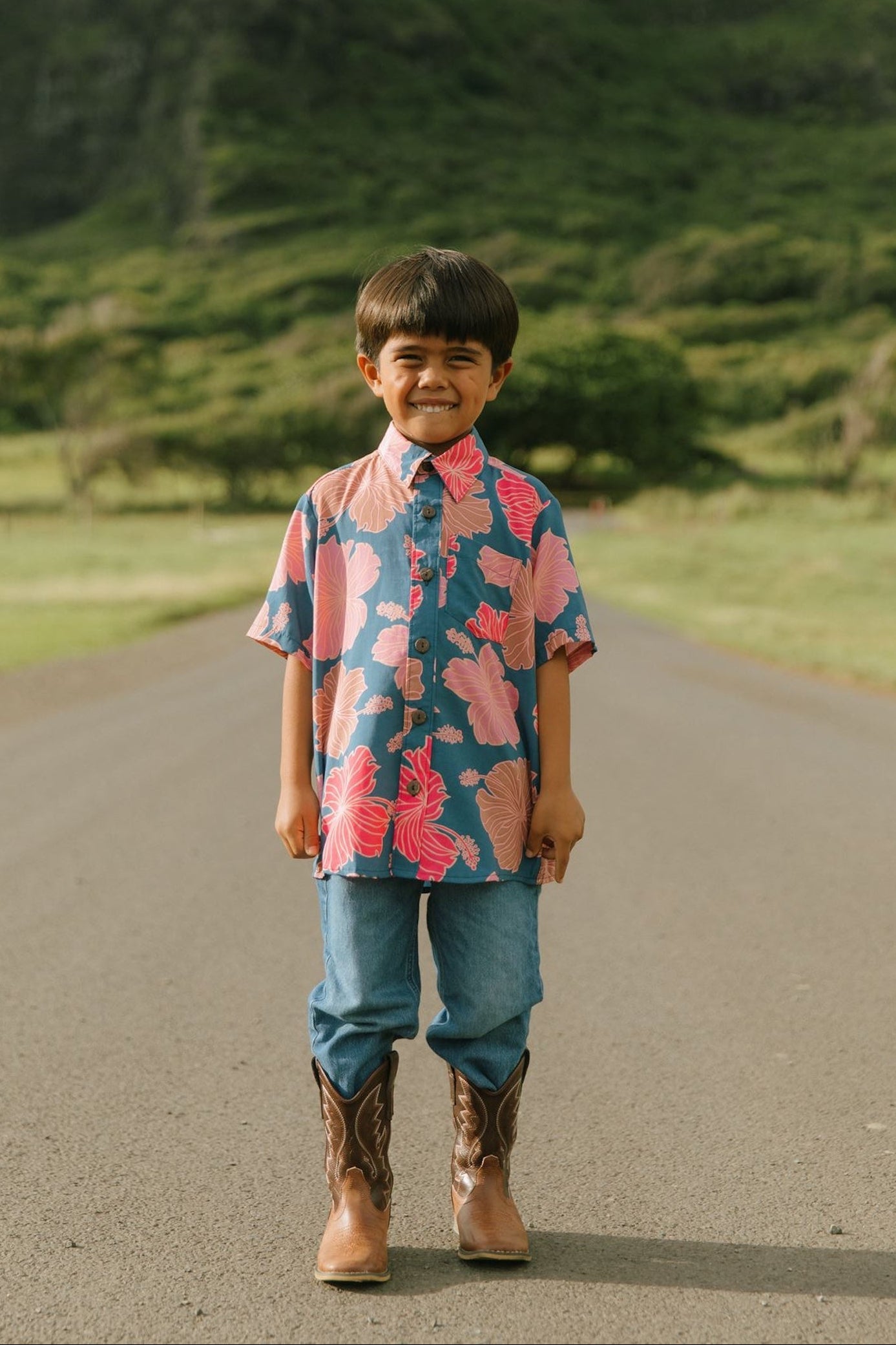 little boy wearing a nevy button up aloha shirt with bright pink hibiscus print