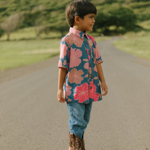 little boy wearing a nevy button up aloha shirt with bright pink hibiscus print