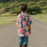 little boy wearing a nevy button up aloha shirt with bright pink hibiscus print