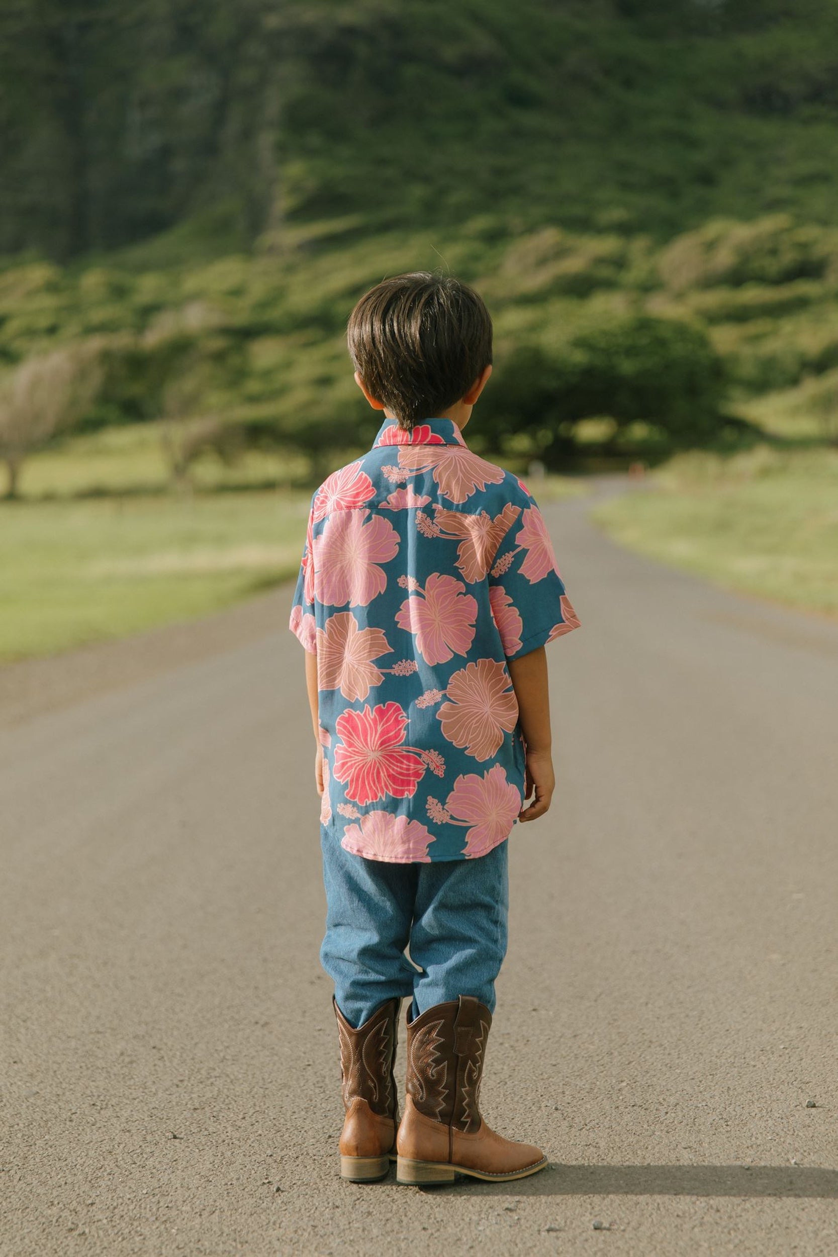 little boy wearing a nevy button up aloha shirt with bright pink hibiscus print