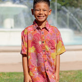 little boy wearing terracotta colored aloha shirt with large purple and yellow flower print 