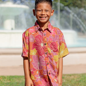 little boy wearing terracotta colored aloha shirt with large purple and yellow flower print 