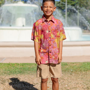 little boy wearing terracotta colored aloha shirt with large purple and yellow flower print 