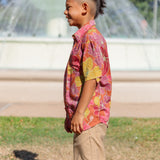 little boy wearing terracotta colored aloha shirt with large purple and yellow flower print 