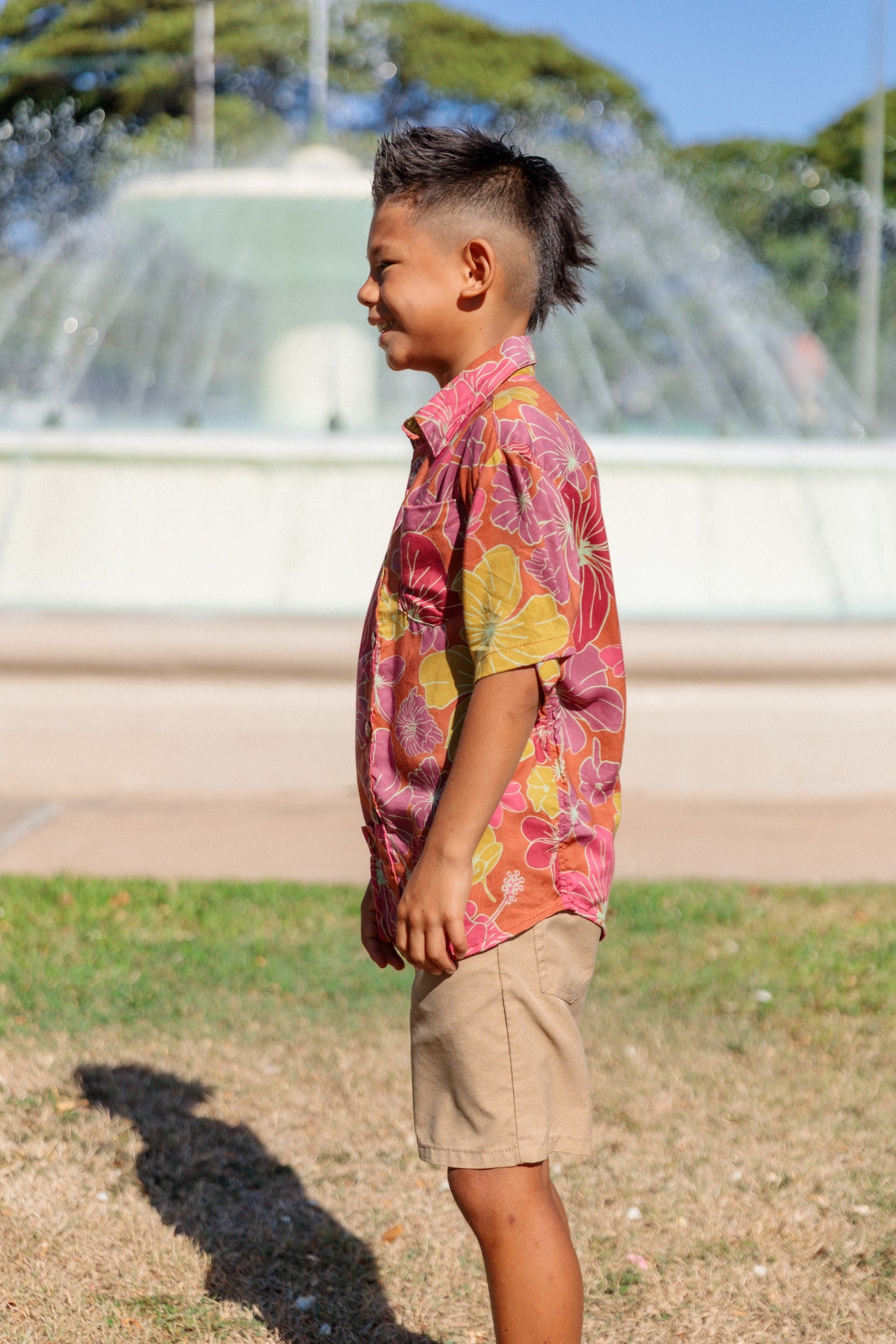 little boy wearing terracotta colored aloha shirt with large purple and yellow flower print 