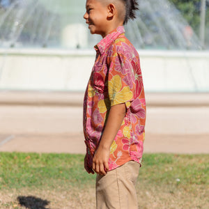little boy wearing terracotta colored aloha shirt with large purple and yellow flower print 