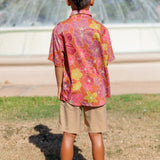 little boy wearing terracotta colored aloha shirt with large purple and yellow flower print 