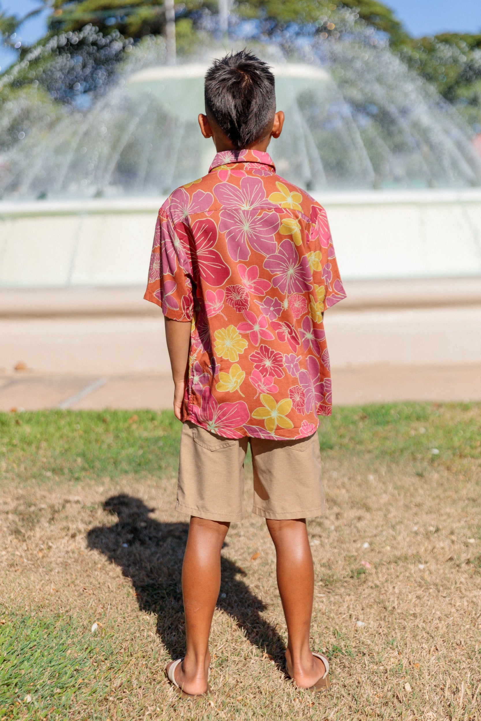 little boy wearing terracotta colored aloha shirt with large purple and yellow flower print 