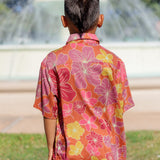 little boy wearing terracotta colored aloha shirt with large purple and yellow flower print 