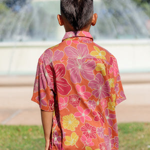 little boy wearing terracotta colored aloha shirt with large purple and yellow flower print 