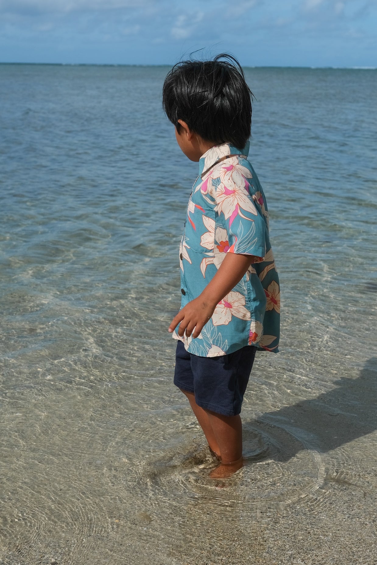 little boy wearing a teal aloha shirt with cream colored orchid blossom pattern