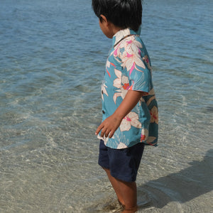 little boy wearing a teal aloha shirt with cream colored orchid blossom pattern