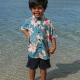little boy wearing a teal aloha shirt with cream colored orchid blossom pattern