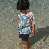 little boy wearing a teal aloha shirt with cream colored orchid blossom pattern
