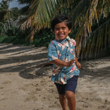 little boy wearing a teal aloha shirt with cream colored orchid blossom pattern