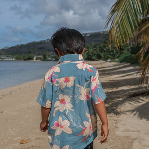 little boy wearing a teal aloha shirt with cream colored orchid blossom pattern