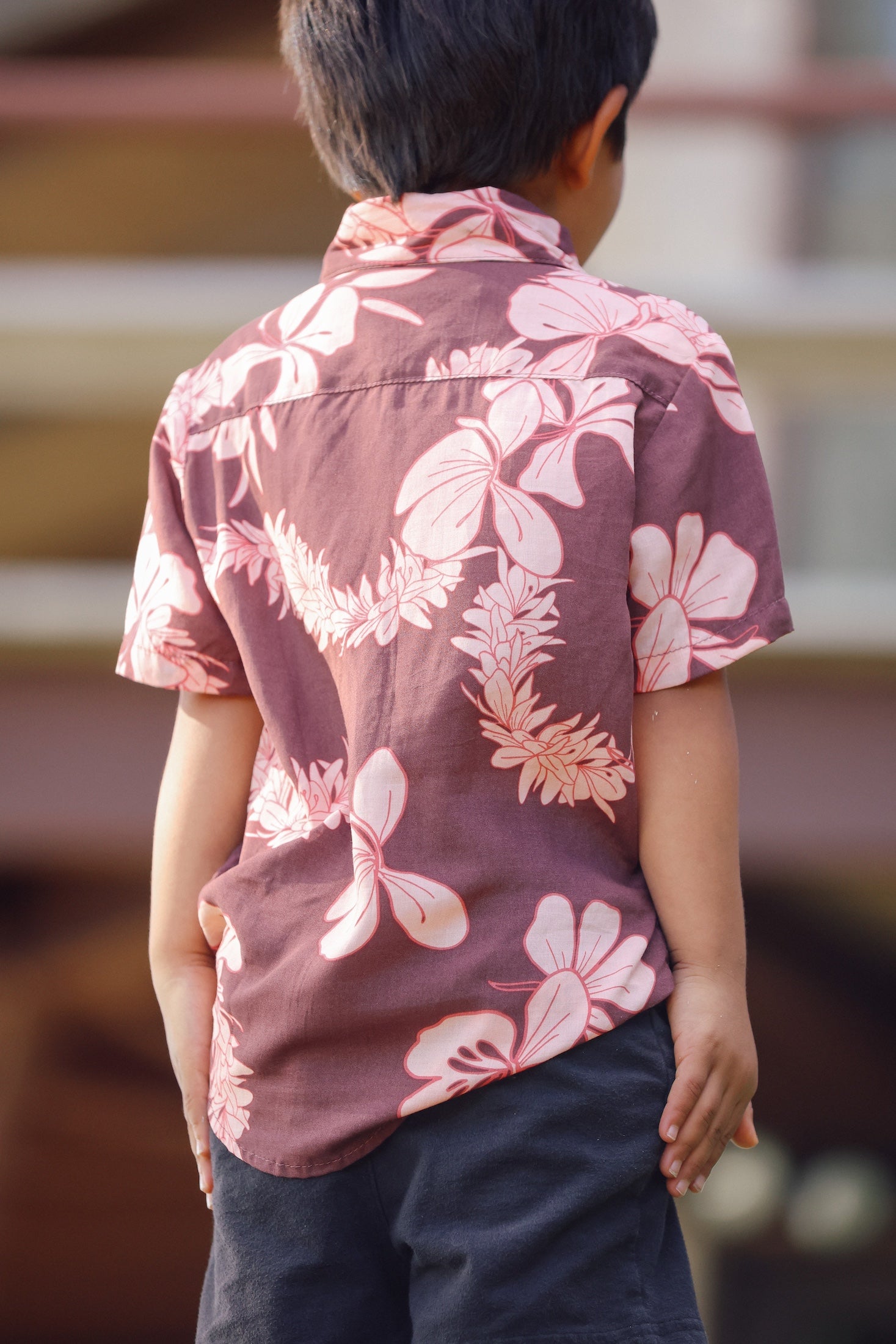 little boy wearing brown aloha shirt with pink lei awapuhi print