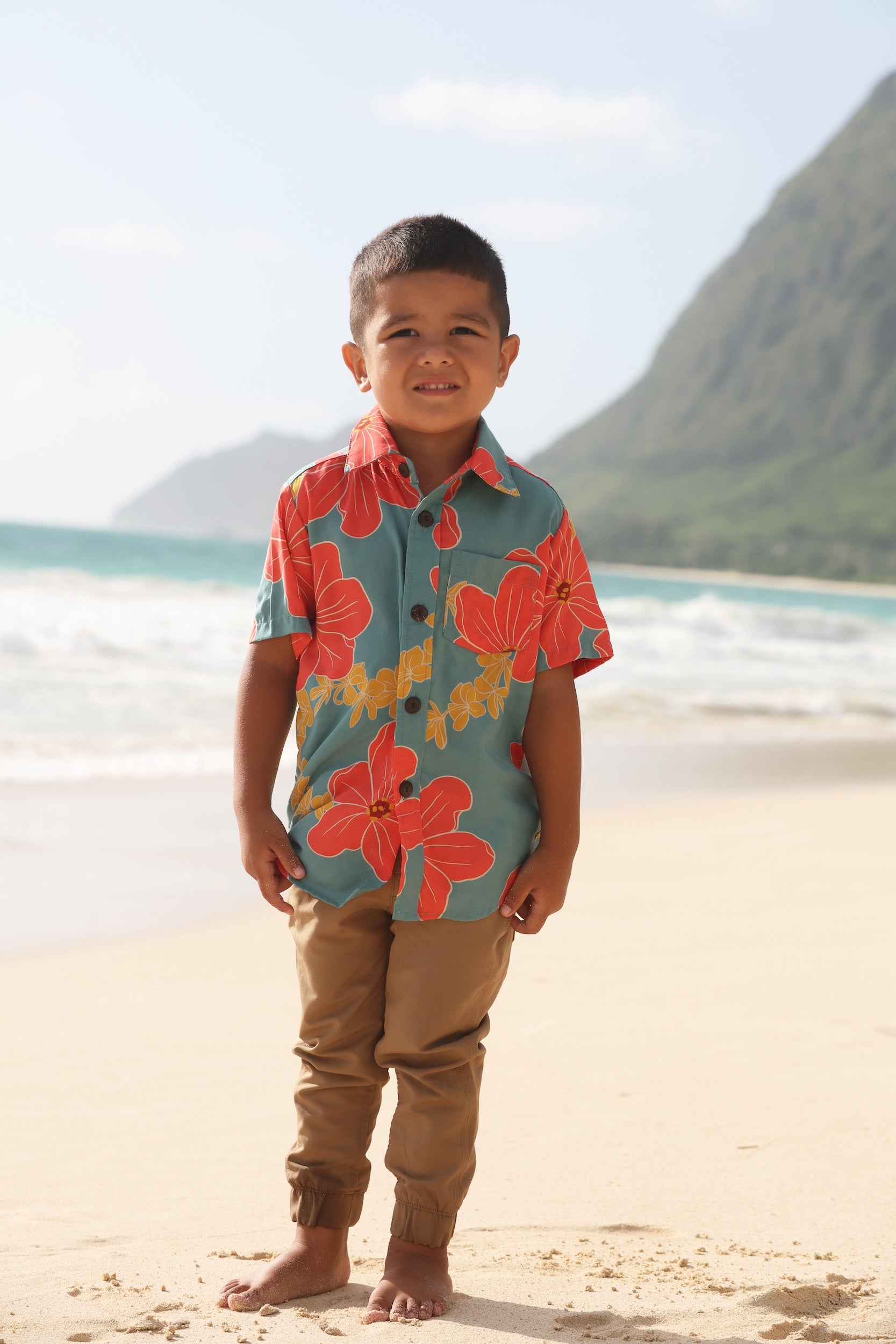 little boy wearing a green button up shirt with orange and yellow lei pua print
