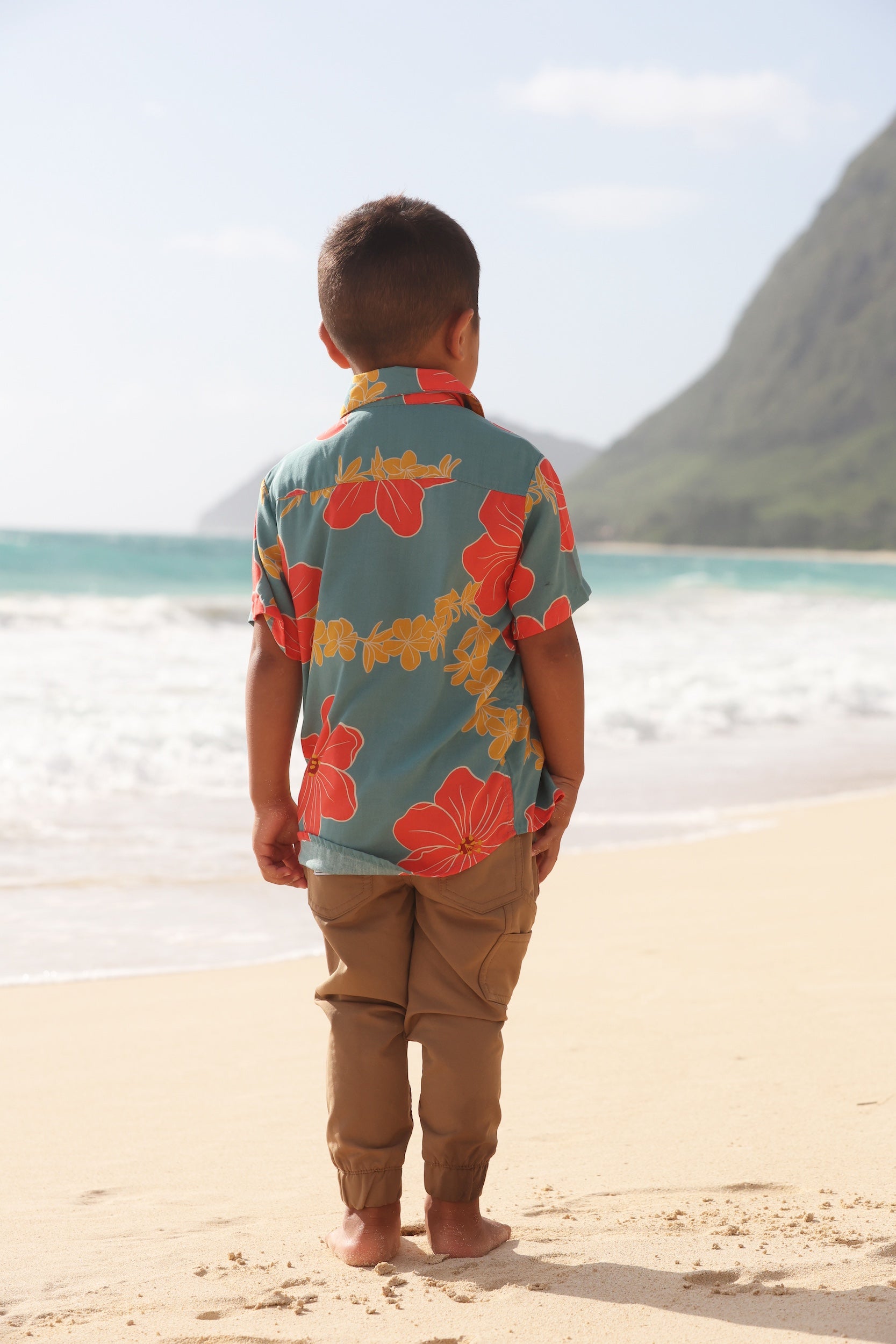 little boy wearing a green button up shirt with orange and yellow lei pua print