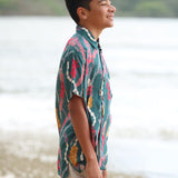 little boy wearing aloha button up shirt in dark teal with shell and lei print