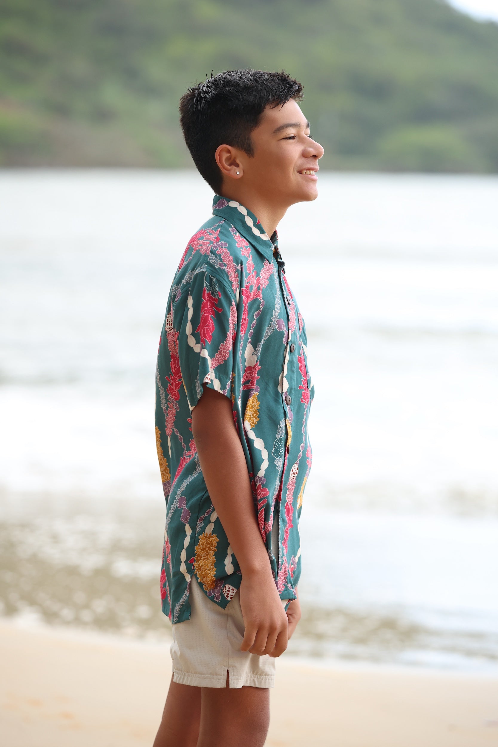 little boy wearing aloha button up shirt in dark teal with shell and lei print