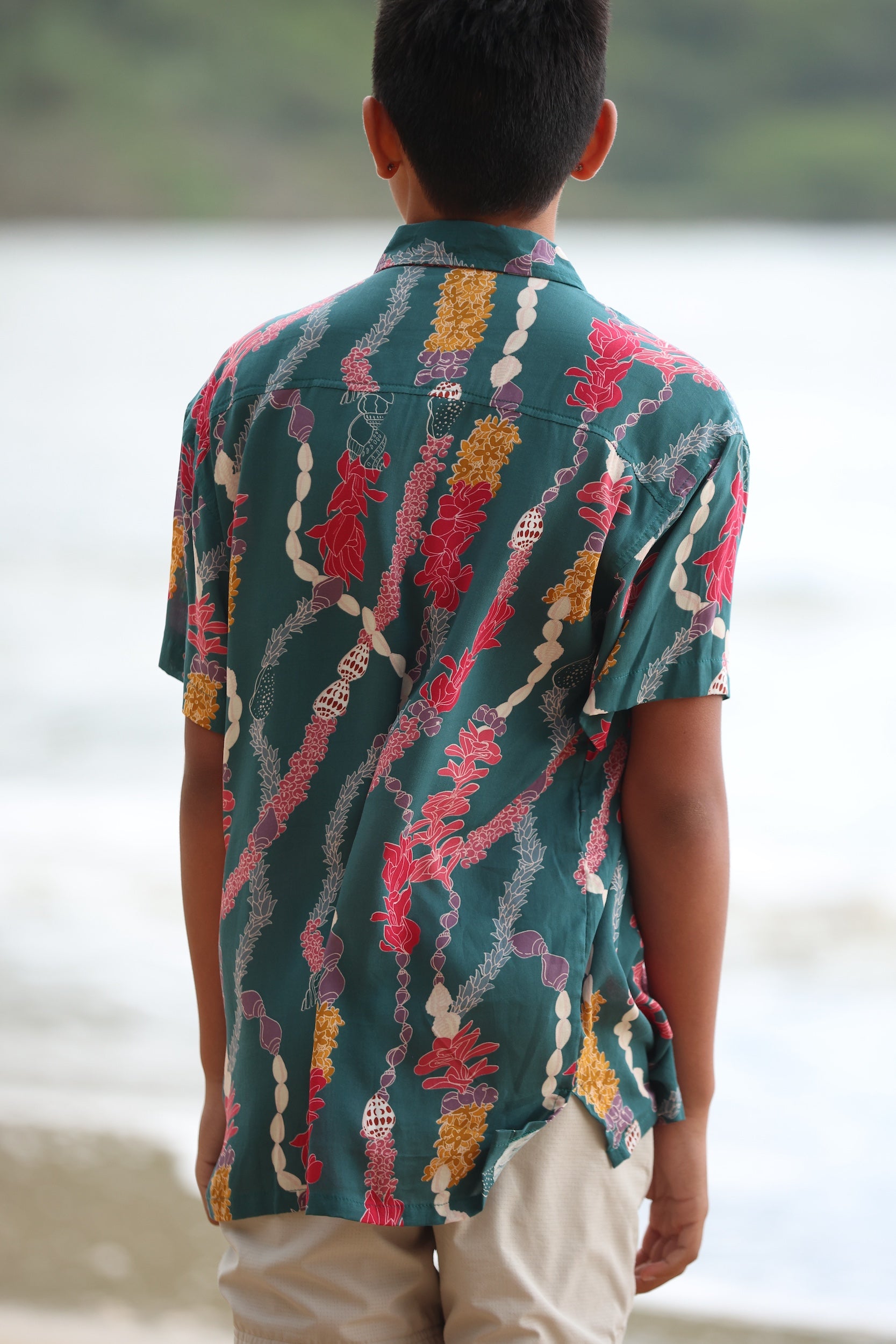 little boy wearing aloha button up shirt in dark teal with shell and lei print