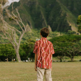 boy wearing red-brown aloha button up shirt with lei print