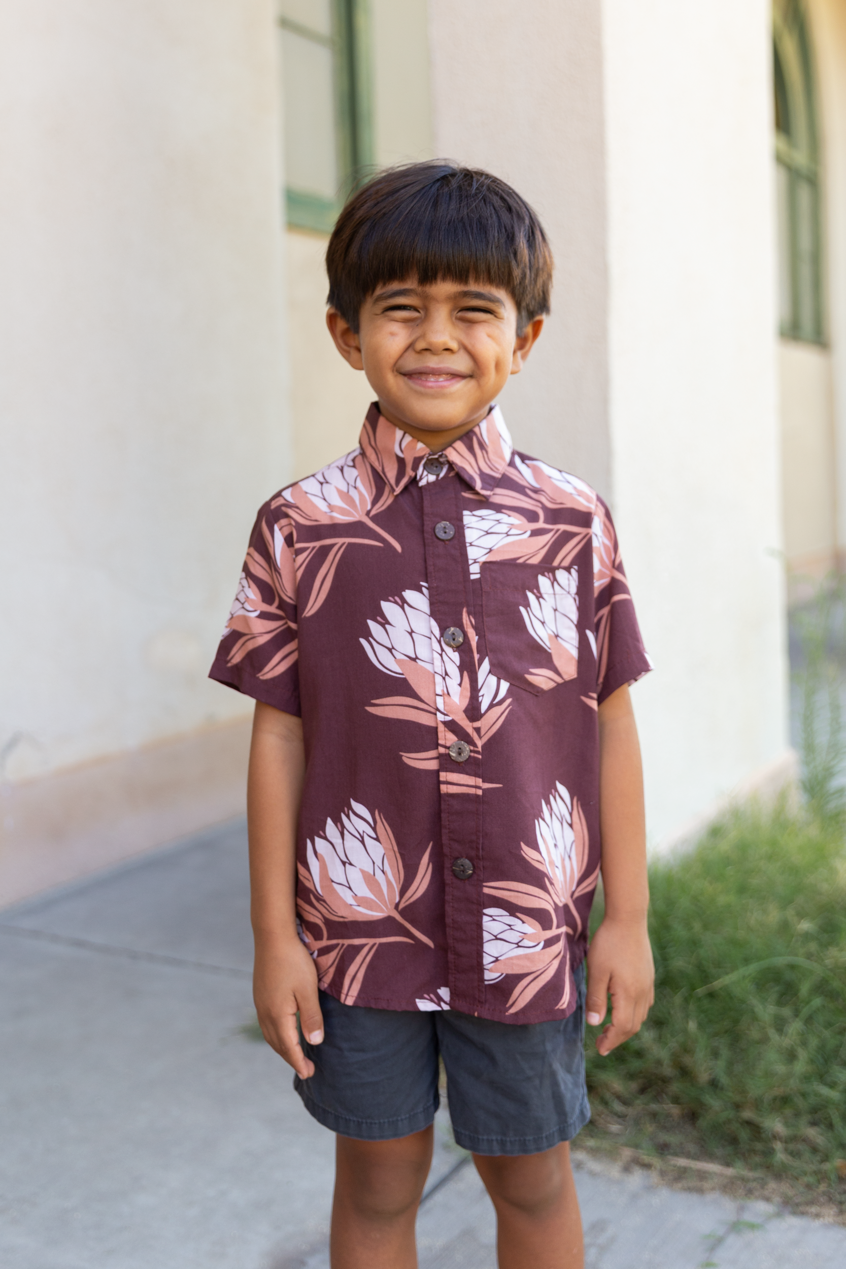 little boy wearing brown mini button up aloha shirt with protea print