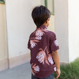little boy wearing brown mini button up aloha shirt with protea print