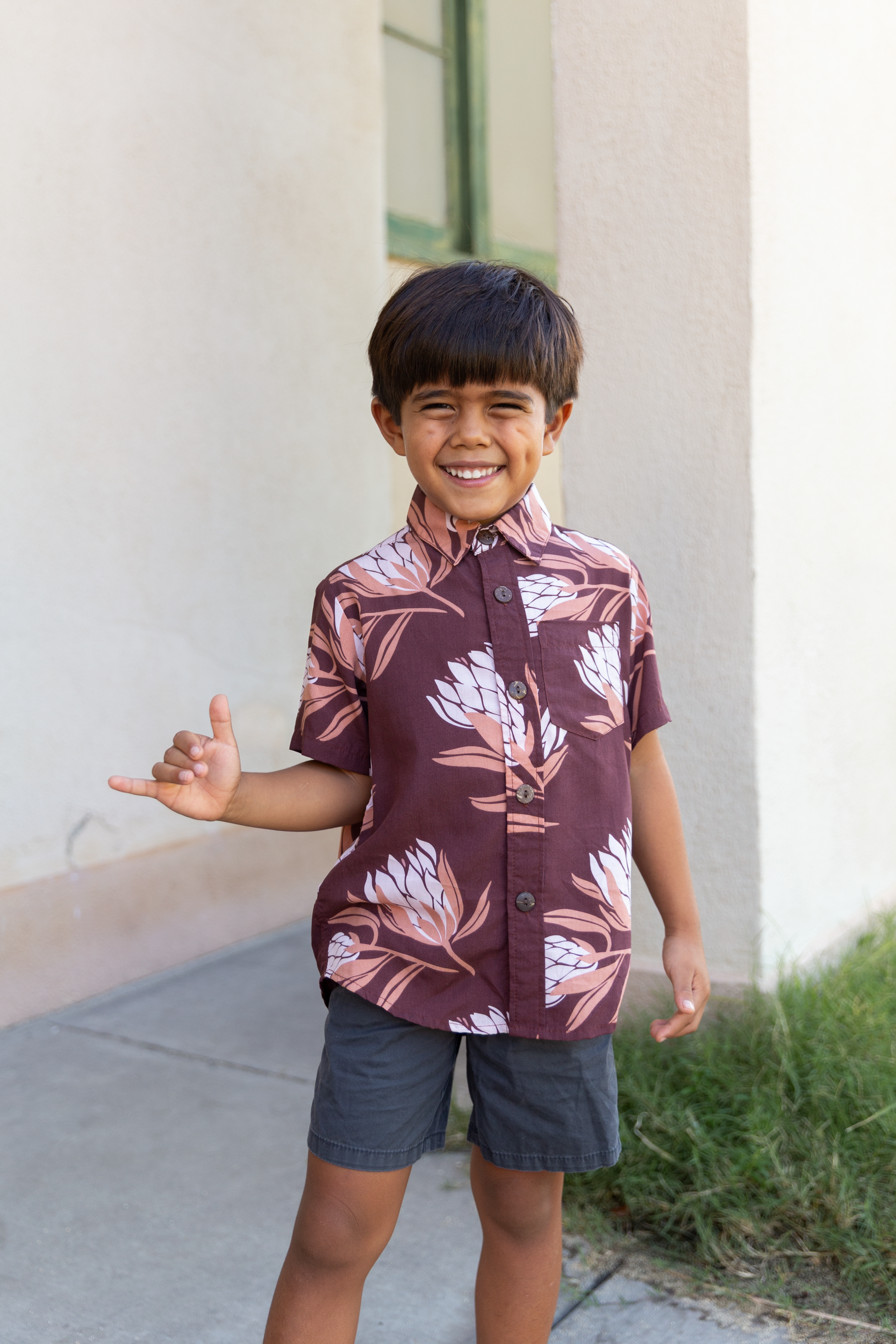 little boy wearing brown mini button up aloha shirt with protea print